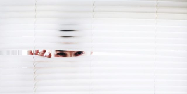 A person looking through a window blind